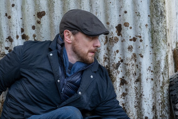 Düz bir şapkayla paslı bir duvarın yanında çömelmiş Edmond Murray rolünde James McAvoy